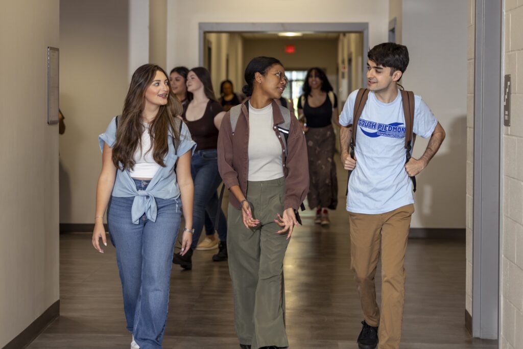 Three students walking down the hallway of South Piedmont chatting with one another.