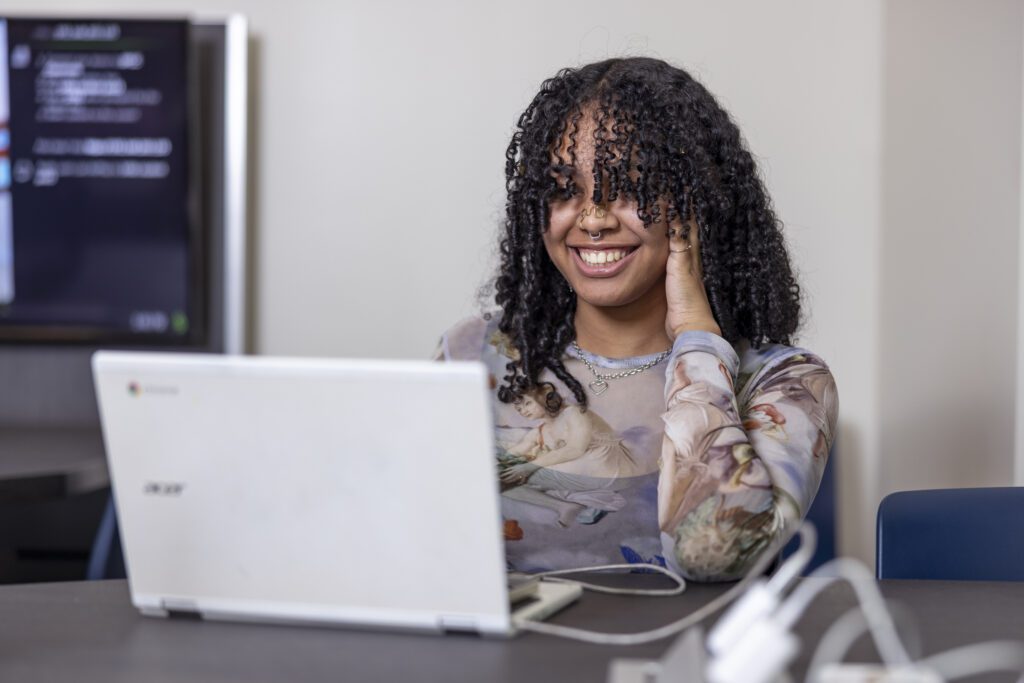 Female student smiling while using a laptop.