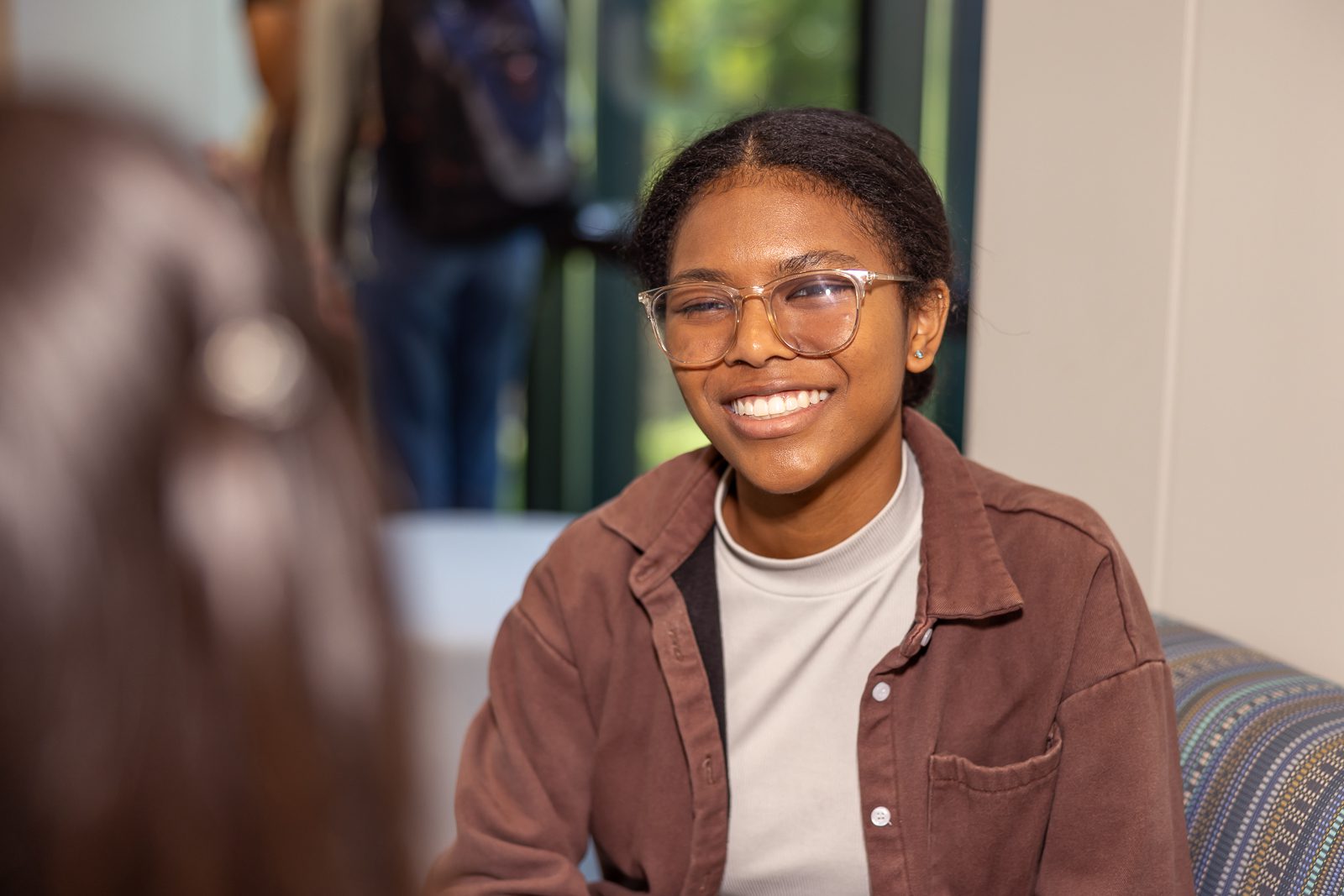 Photo of a female student in a brown jacket smiling at the camera.