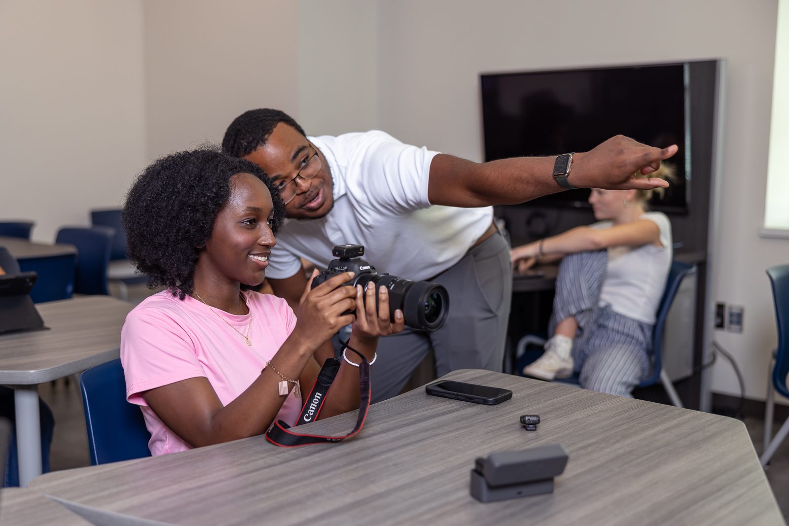 Photo of a male student showing a female student how to use a camera.